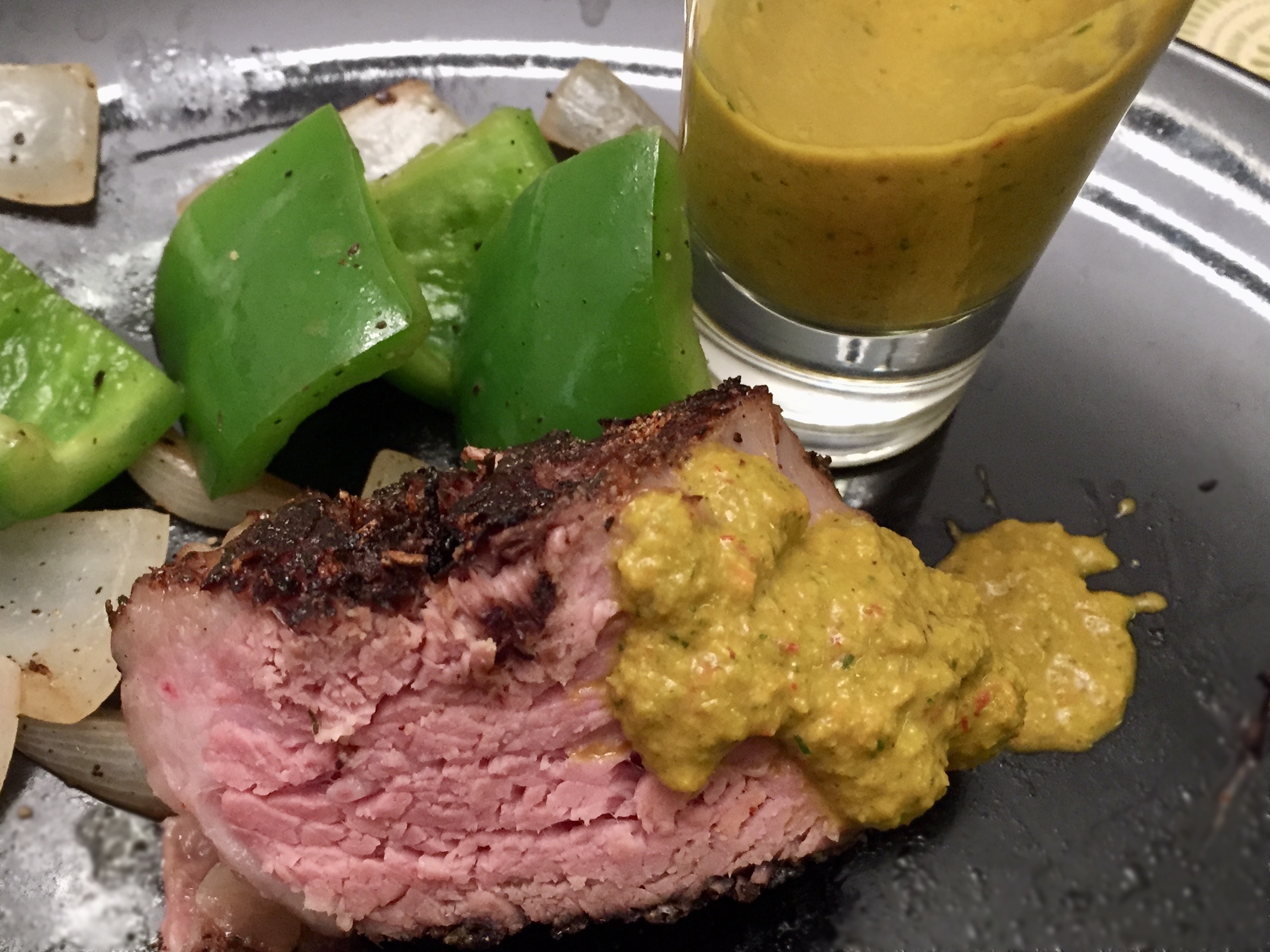 Yellow sauce with flecks of red and green on steak, with a side of bell peppers and onions.